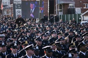 Law enforcement officers turn their backs on a live video monitor showing New York City Mayor Bill de Blasio has he speaks at the funeral of slain New York Police Department (NYPD) officer Rafael Ramos in New York